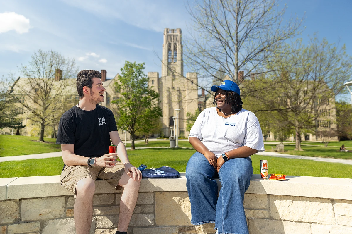 Two people are smiling and chatting while sitting outdoors on a sunny day.