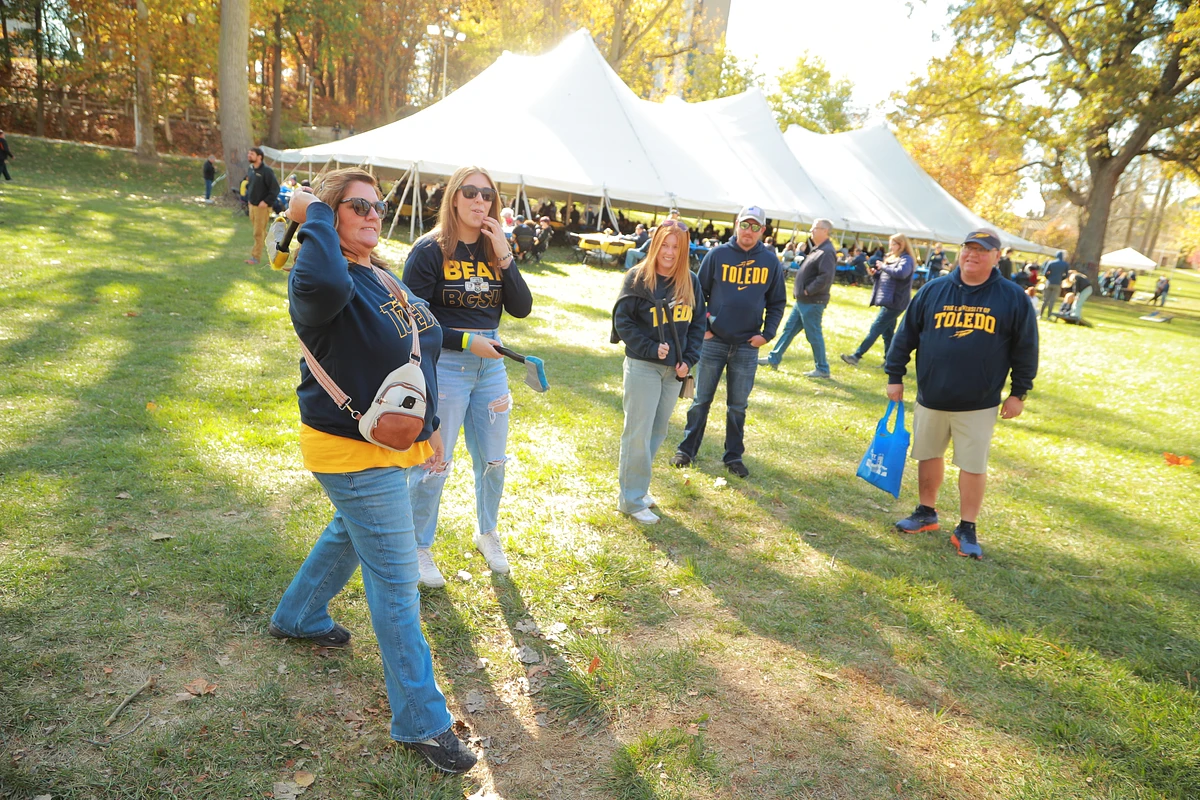A group of people wearing Toledo-themed clothing stand in a grassy area near a tent on a sunny day.