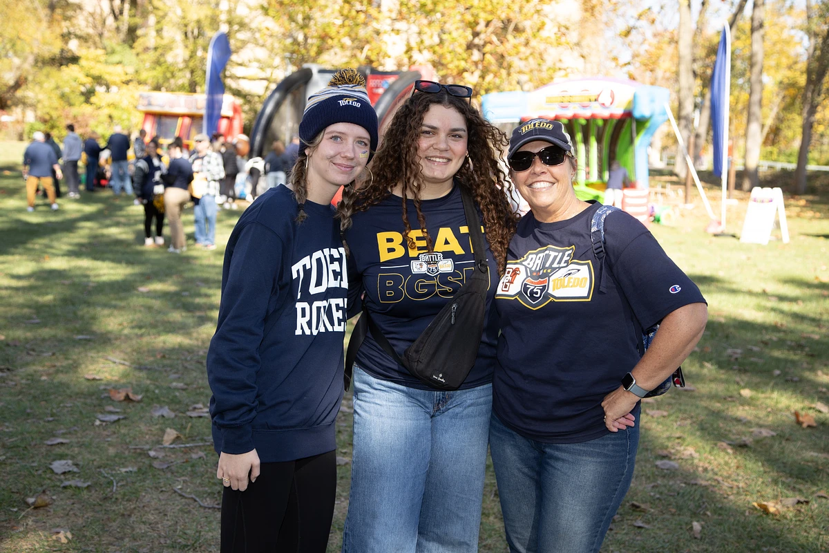 Three people wearing Toledo-themed clothing pose together outdoors at an event.