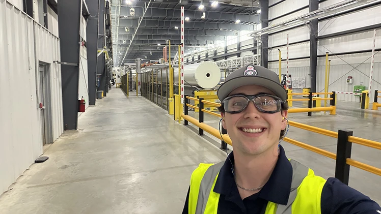Smiling worker in a factory with a yellow barrier.