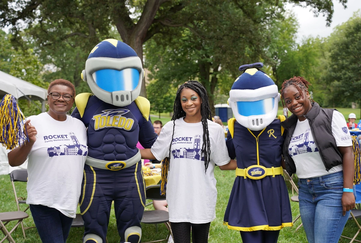 Five people posing with two mascots in an outdoor setting.